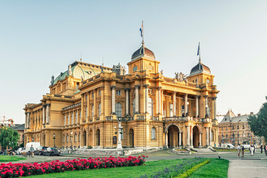 Golden hour sunlight bathes the elegant historic theater opera house of Zagreb with people milling around its entrance amidst vibrant city life, Zagreb, Croatia