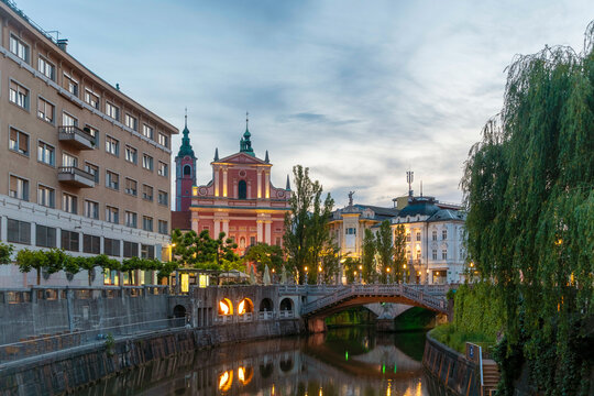 Evening view of tranquil Ljubljana River with a bridge and Franciscan Church of the Annunciation in the background, Ljubljana, Slovenia