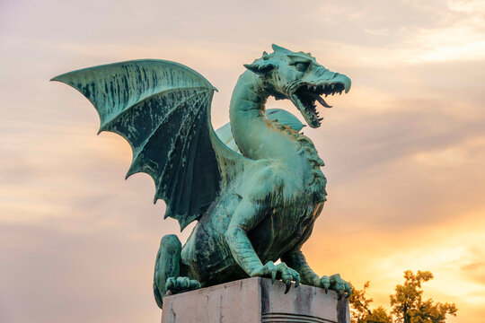 A green dragon statue with outstretched wings against a twilight sky on the Dragon Bridge in Ljubljana, Slovenia