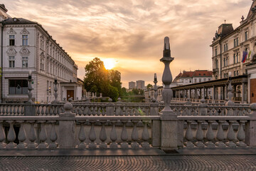 Sunrise over a European cityscape with classical architecture and an ornate balustrade along a triple bridge or promenade, Ljubljana, Slovenia