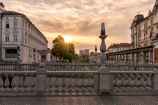 Sunrise over a European cityscape with classical architecture and an ornate balustrade along a triple bridge or promenade, Ljubljana, Slovenia
