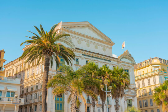 Sunlit elegant building o fthe Opera House with classical architecture are framed by a palm tree under a clear blue sky, Nice, France