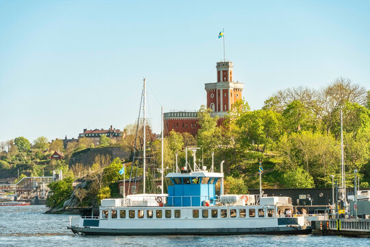 Passenger ferry named Djurgarden 9 in front of the lush greenery and historic stockholm castle, Stockholm on a clear day, Sweden