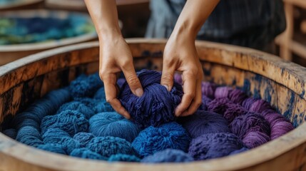 Hands arranging colorful blue and purple yarn in wooden barrel