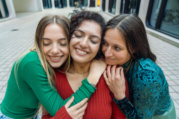 Three smiling women embracing each other in a close huddle, radiating happiness and friendship, Berlin, Germany