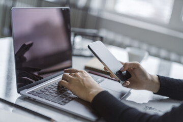Woman deeply focused on her modern smartphone, laptop in the background within a softly blurred office setting