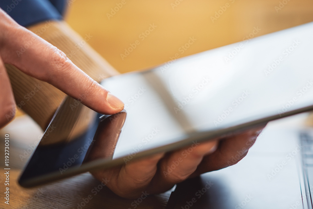 Poster closeup view of a man's finger operating a high-tech tablet on a desk, amidst the blurred backdrop o