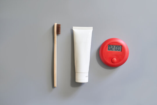 Eco friendly bamboo toothbrush with toothpaste tube and red digital timer on gray background.