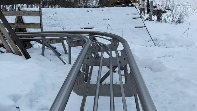 Metal rollercoaster tracks winding through snow blanketed winter terrain, revealing dramatic curves and exhilarating descents across frozen landscape with intense perspective