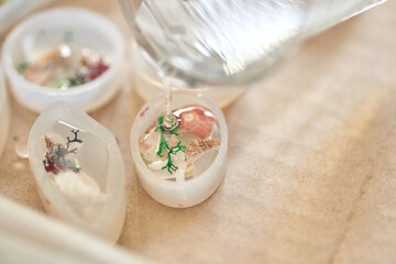 Crafting resin art with dried flowers and shells in molds on beige surface.