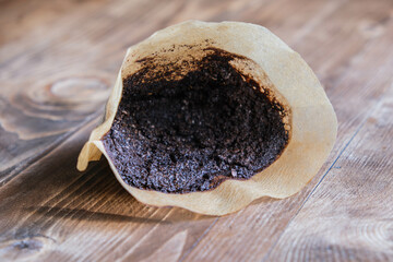 Used cone coffee filter on a wooden table, used ground coffee in a filter