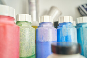 Colorful array of plastic paint bottles in a row on shelf closeup with focus on shapes and textures.