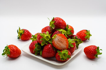 Pile of fresh strawberries in a ceramic plate on a white background.