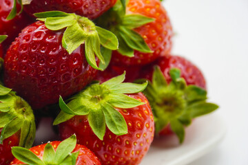 Close-up macro shot of ripe, juicy strawberries with vibrant green leaves on a white surface