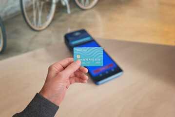 A hand holding a credit card over a POS terminal, symbolizing contactless payment in shops. A classic payment method in modern commerce