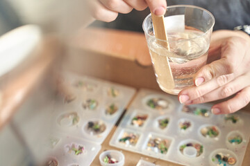 Close up of hands stirring resin with molds for crafting jewelry and decorations in creative workshop.