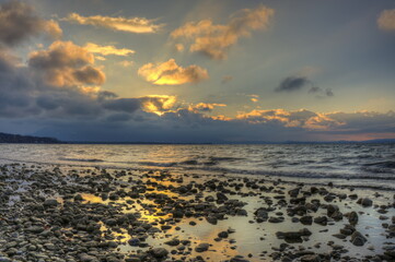 Sonnenuntergang am Chiemsee mit Steinen am Strand und Wolken am Horizont