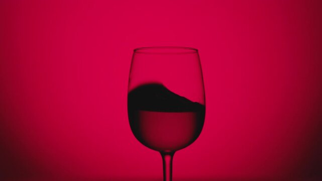 A striking silhouette of a wine glass with liquid swirling inside, set against a bold red background, creating a dramatic and modern aesthetic of elegance and refinement