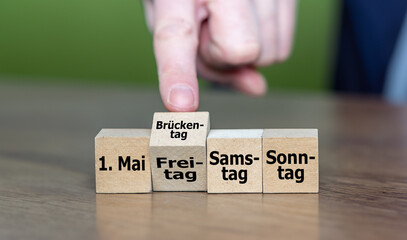 Symbol für einen Brückentag. Hand dreht Würfel und ändert das Wort 'Freitag' in 'Brückentag'.