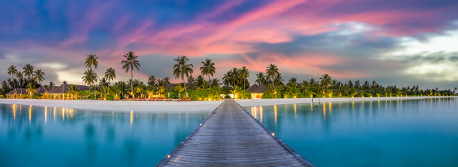 Amazing sunset panorama Maldives tourism. Luxury resort wooden pier with soft led lights under colors sky. Beautiful twilight clouds over fantastic beach sea shore background for vacation holiday