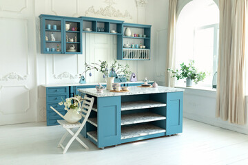 Stylish cuisine with flowers in vase. Kitchen utensils on table. Kitchen island in dining room. Branches olive tree in vase with easter eggs. Blue kitchen interior with furniture and easter decor.	
