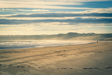 A distant couple silhouette on the beach, with the sun low in the sky casting a golden light over Cruden Bay Beach, Aberdeenshire, Scotland on a cold New Year's Day.