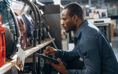 Holding tablet, looking at vacuum cleaners. Worker is in the home appliance store