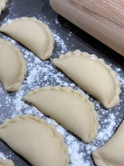 Homemade vareniki on a floured table with a wooden rolling pin