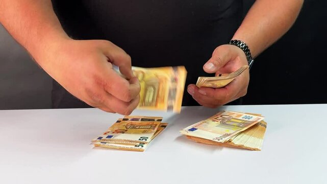 A person is sorting and organizing Euro bills into separate stacks on a table. The individual carefully counts each bill, ensuring proper organization.