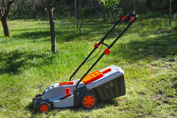 Gray and orange electrical mower on the grass in a sunny day