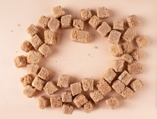round frame of brown sugar pieces on beige background, copy space