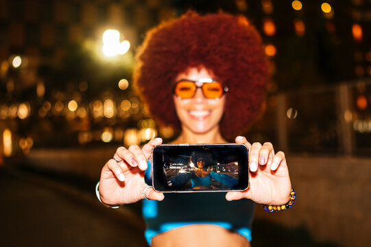 Woman with afro hair holding smartphone, nighttime scene