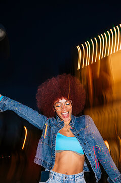 Joyful African descendant woman with afro hair dancing at night