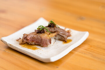 Wagyu beef sushi garnished with herbs and sauce, served on a minimalist white ceramic plate.