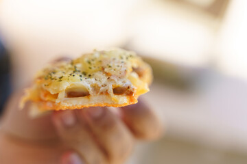 Closeup of a bite-sized cheesy pizza slice with toppings and herbs in hand.