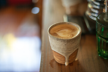 Artisanal coffee with latte art served in a handmade ceramic cup on a wooden table.