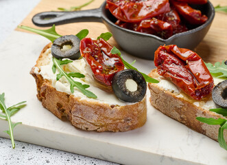 Sandwich with cream cheese and sun-dried tomato slices on white table