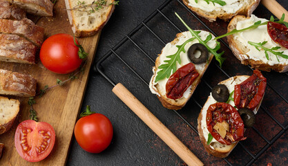 Ciabatta spread with cream cheese, topped with wedges of dried tomatoes with spices on the table,...