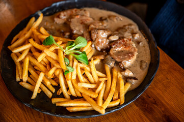 Turkey meat piece in spicy vegetable and mushroom sauce with french fries on black plate.