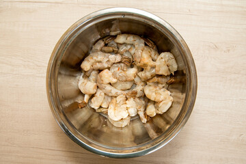marinated raw shrimp.Hands holding a stainless steel bowl full of Shrimps have visible spices, ready to cook. Slightly out of focus background,