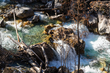 Mountain river flows in turbulent foaming stream in stone bed between huge boulders. Pure emerald...