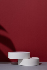Geometric white scene with the shadow of a monstera leaf on a gray and burgundy background. A premium podium for advertising and presentation of your product. Showcase, display case.
