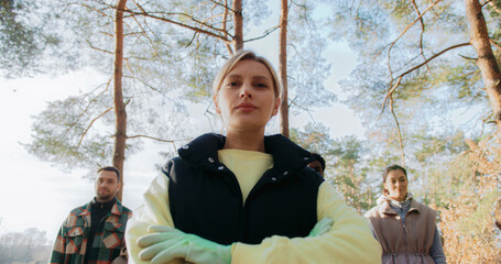 Obraz premium Serious woman looking at camera after collecting plastic. Cleaning up nature from plastic waste. Bags with trash located on ground. Woman crossing her hands.