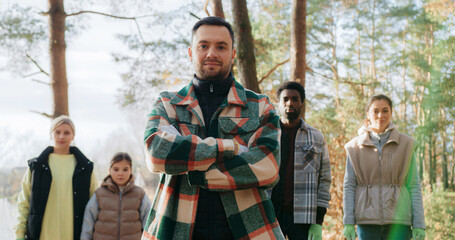Front view of people standing in line and looking at camera. Man in front crossing his hands while smiling. Wearing warm checkered shirts. Colleagues proud of cleaning up nature from plastic waste.