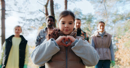Little girl in middle making heart symbol with both hands in front of her chest.