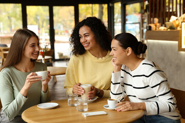 Happy women with coffee drinks chatting in cafe