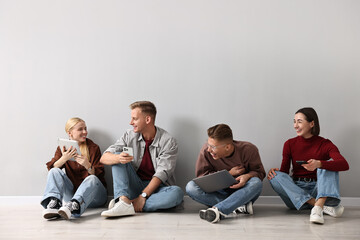 Fototapeta premium Group of people using different gadgets near light grey wall indoors. Modern technology