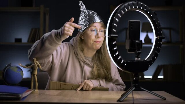 Strange crazy blogger with cellphone, paranoid woman streaming at home conspiracy theory broadcasting in vlog, telling about fake news showing text on camera. blogging, technology and people