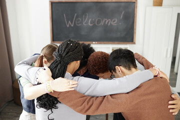 Diverse group of teenage children embracing while standing in circle during group therapy and...