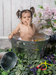 A little girl playing in a copper bathtub or bathing basin with a retro design, surrounded by rubber bath toys. A playful and cozy scene evoking childhood memories.
